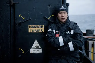 A crew member of the M/V Steve Irwin stands resolutely in front of a warning-laden door on the Southern Ocean, embodying the ship’s mission of marine conservation.