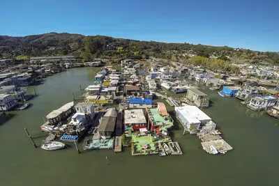 A vibrant aerial view of Sausalito’s Gate 6 Houseboat Co-Op, showcasing colorful floating homes nestled in calm waters beneath a clear blue sky.