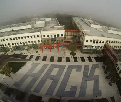 A foggy aerial view of the HACK courtyard at Facebook Headquarters, featuring bold ground lettering and modern buildings with red structural accents.