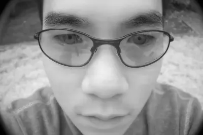 A close-up black-and-white self-portrait of a young man with glasses, captured in infrared at dawn, showing intense eyes and a contemplative expression.